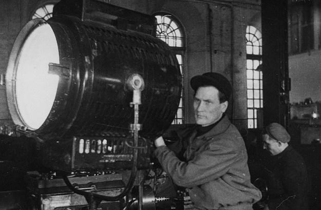 Filmivõtted tehases Volta. Valgustaja Enn Erm lülitab sisse prožektori - valmimas on dokumentaalfilm „Taassündinud tehas“ (1949). Kaader kinokroonikast „Päev Tallinna Kinostuudios“ (1950), Ringvaade „Nõukogude Eesti“ nr 4, 10. veebruar 1950, 3/4